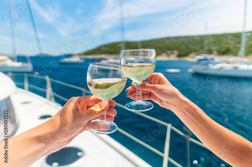 Couple holding two glasses of white wine over ocean background with yacht on background