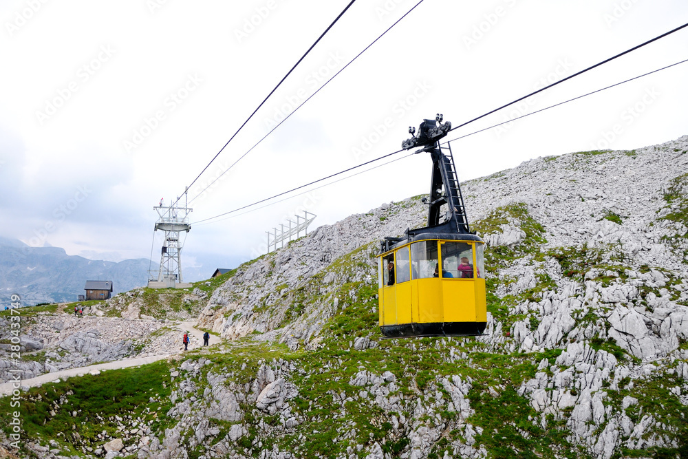 Cableway in the mountains. Yellow cab with people riding a cable car. People walk along the path up to the cable car.