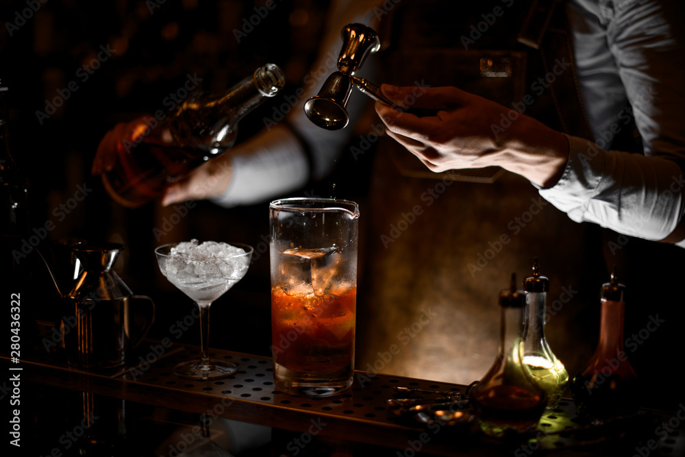Bartender pours alcohol cocktail using jigger with handle