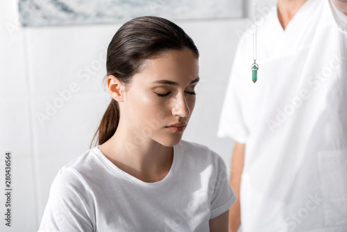 cropped view of hypnotist standing near woman and holding green stone near her face photo