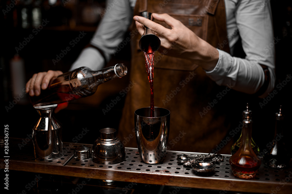 Close shot of bartender pouring alcohol from jigger to shaker