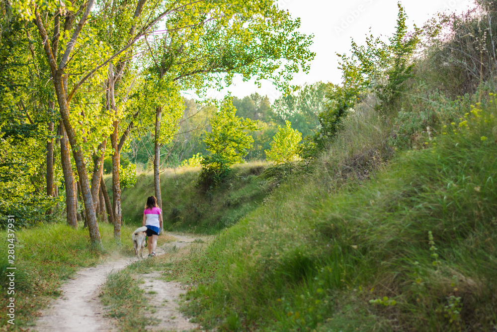 Middle-aged woman walking with her dog on a mountain path Middle-aged woman walking with her dog on a mountain path