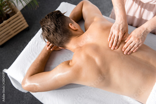 cropped view of masseur and shirtless man lying on massage table