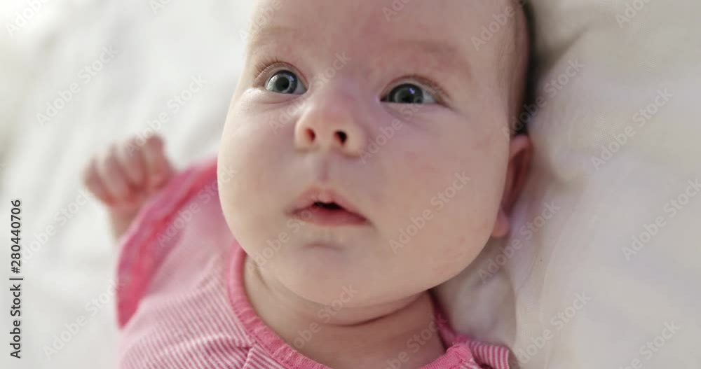 From above video of cute cheeky female infant wearing pink shirt lying on back on bed and looking around with opened mouth From above video of cute cheeky female infant wearing pink shirt lying on back on bed and looking around with opened mouth