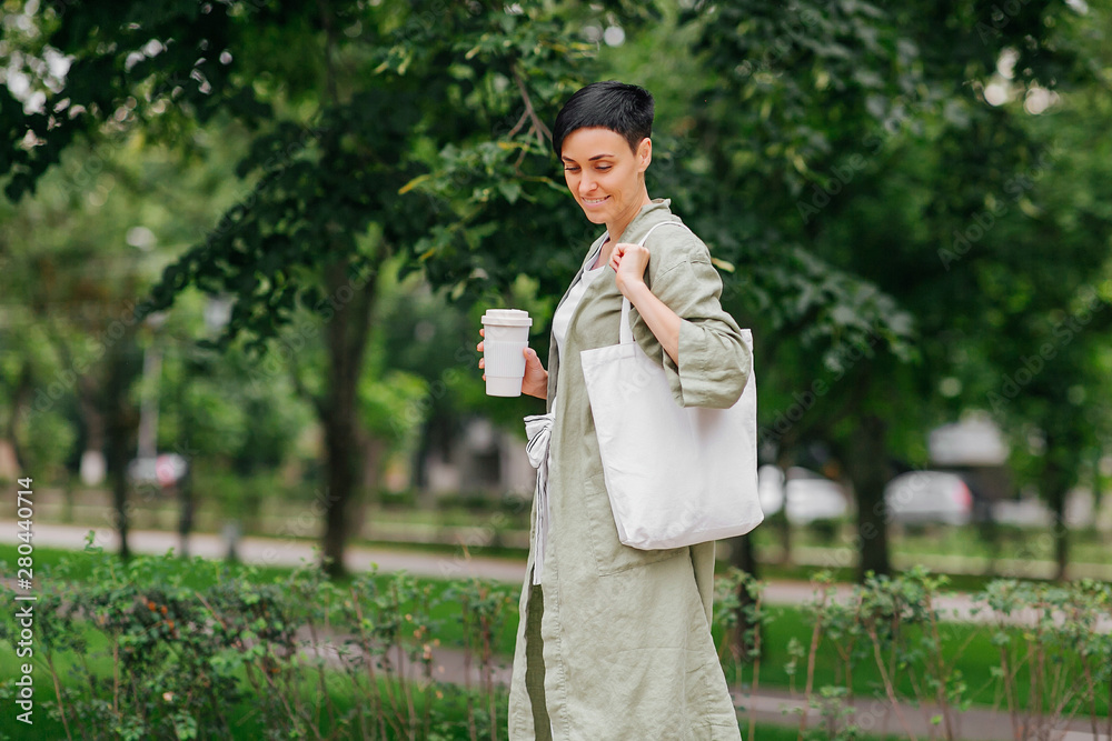 Woman with short hair holding reusable coffee cup and eco bag enjoying morning. Eco friendly concept. Woman with short hair holding reusable coffee cup and eco bag enjoying morning. Eco friendly concept.