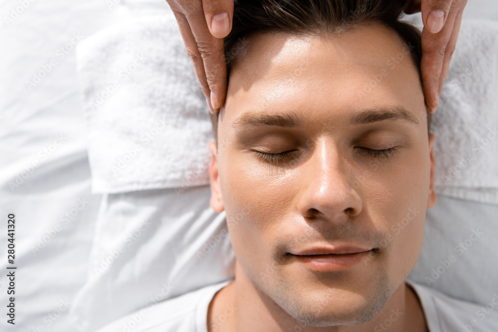 cropped view of masseur standing near man with closed eyes and touching his head cropped view of masseur standing near man with closed eyes and touching his head