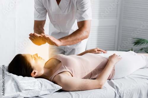 cropped view of healer standing near woman on massage table and cleaning her aura
