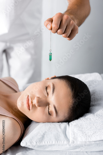 cropped view of hypnotist standing near woman on pillow and holding green stone
