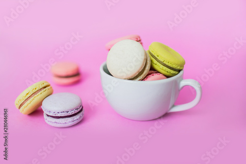 Creative image of sweet colorful French macaroon biscuits in a white mug on pink background.