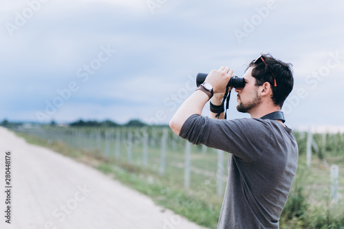 Portrait of young adventure man travelling with binoculars, watching landscape view outdoors. Young brunette man discover nature scenes. Travelling, discovering, vacation concept