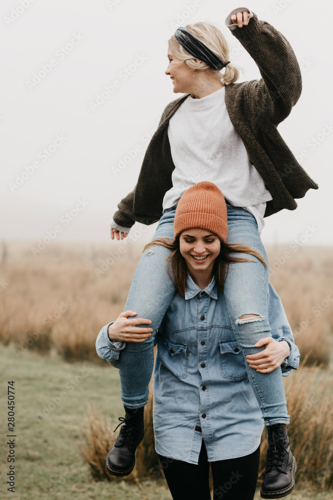 UK, Scotland, Isle of Skye, happy woman carrying friend piggyback in rural landscape
