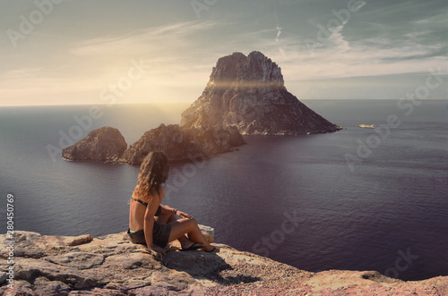 Amazing seascape view with a girl looking ahead to the magic rock of Es Vedra Island at sunset. Summertime in Cala d'Hort, Ibiza, Balearic Islands.