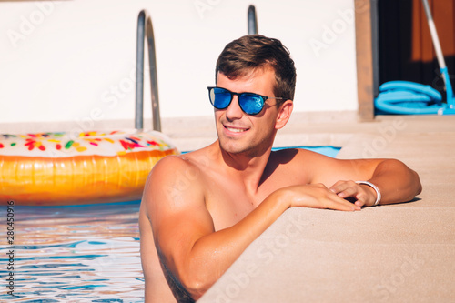 Handsome young man with sunglasses enjoying deserved vacation in pool photo