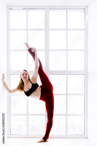 Yoga girl in red tights near the window on a white background © Vasil