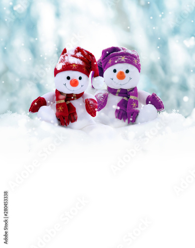 Two little snowmen the girl and the boy in caps and scarfs on snow in the winter. Background with a funny snowman. Christmas card.