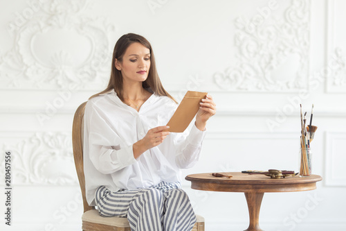 A young beautiful girl in a luxurious interior sits on a chair, holds a letter in her hands and reads it. Soft focus.