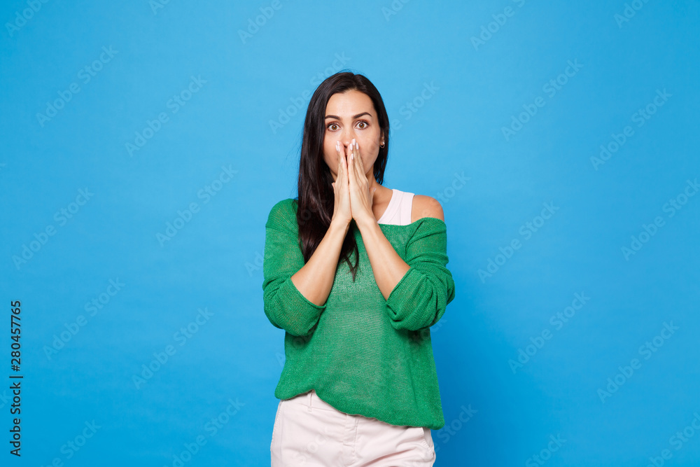 Portrait of shocked amazed young woman in green casual clothes looking camera covering mouth with hands isolated on bright blue wall background in studio. People lifestyle concept. Mock up copy space. Portrait of shocked amazed young woman in green casual clothes looking camera covering mouth with hands isolated on bright blue wall background in studio. People lifestyle concept. Mock up copy space.