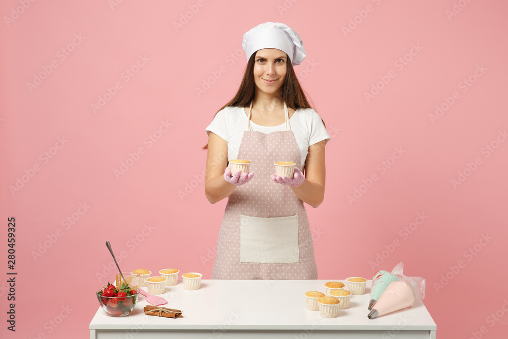 Cute housewife chef cook confectioner or baker in white t-shirt, toque chefs hat cooking at table isolated on pink pastel background in studio. Cupcake making process. Mock up copy space food concept. Cute housewife chef cook confectioner or baker in white t-shirt, toque chefs hat cooking at table isolated on pink pastel background in studio. Cupcake making process. Mock up copy space food concept.