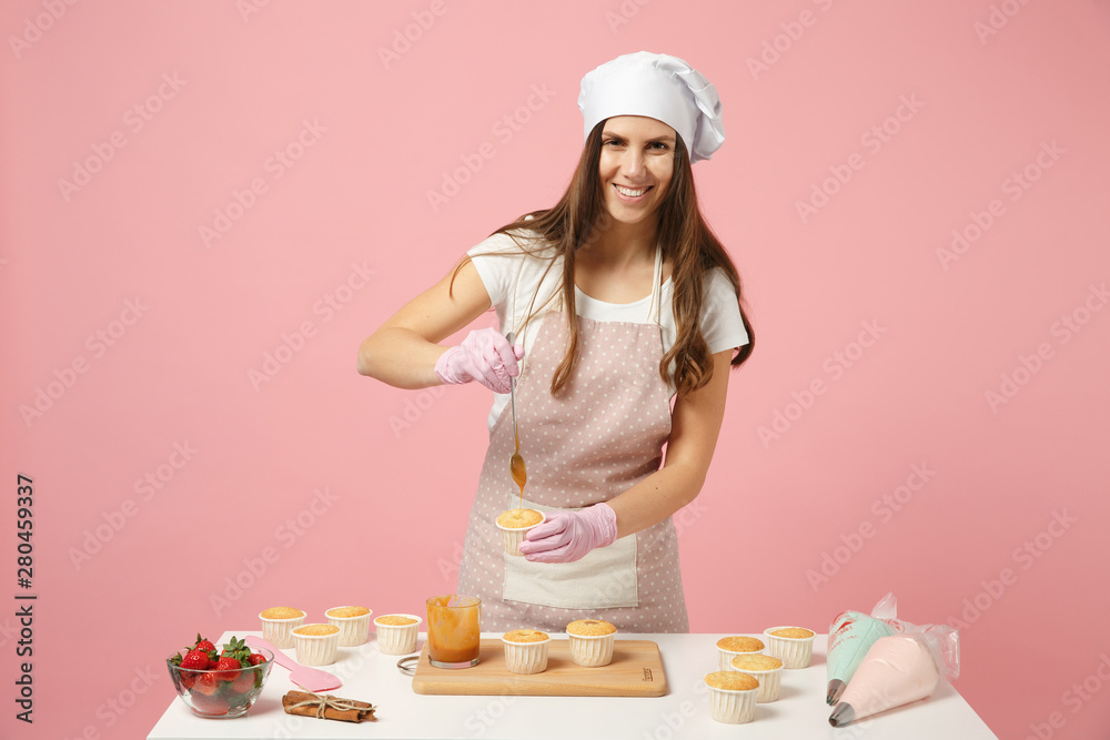 Cute housewife chef cook confectioner or baker in white t-shirt, toque chefs hat cooking at table isolated on pink pastel background in studio. Cupcake making process. Mock up copy space food concept. Cute housewife chef cook confectioner or baker in white t-shirt, toque chefs hat cooking at table isolated on pink pastel background in studio. Cupcake making process. Mock up copy space food concept.