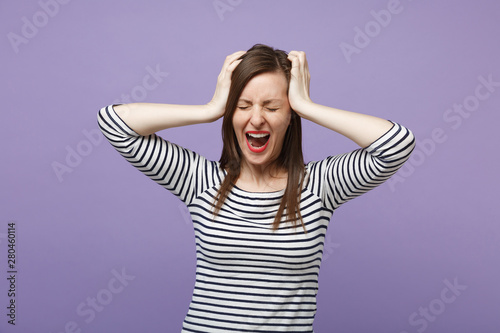 Frustrated woman in casual striped clothes posing isolated on violet purple background in studio. People lifestyle concept. Mock up copy space. Keeping eyes closed, screaming, putting hands on head.