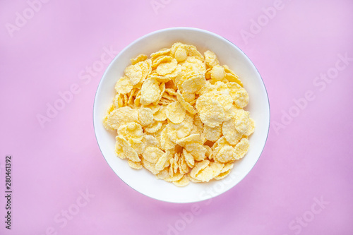 Cornflakes dry breakfast in a white bowl on a pink backgroud. top view