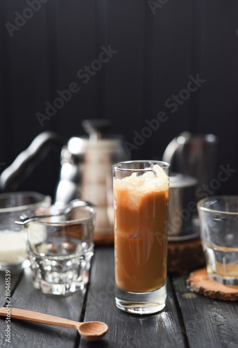 Iced coffee with cream in tall glass on black background copy space