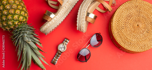 Flat lay, Wicker fashion bag, sunglasses, tropical pineapple and expensive watches and women's shoes. Summer fashion, the concept of the holiday. On a bright red background. photo