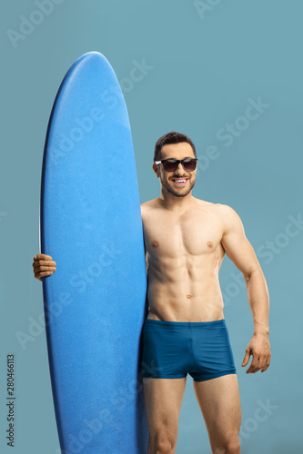 Young muscular guy holding a surfing board