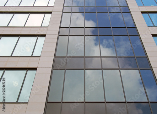 upwards view of the facade of a modern office buildings with blue sky and white clouds reflected in the rows of geometric windows