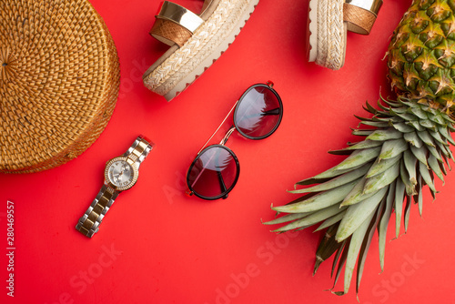 Flat lay, Wicker fashion bag, sunglasses, tropical pineapple and expensive watches and women's shoes. Summer fashion, the concept of the holiday. On a bright red background.