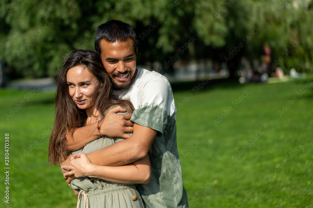 Mixed couple in love is hugging in park during warm summer sunny weather. friend and girlfriend different races love each other. Tolerance, world peace. Lifestyle Mixed couple in love is hugging in park during warm summer sunny weather. friend and girlfriend different races love each other. Tolerance, world peace. Lifestyle