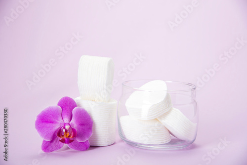 Cotton sponges in a glass jar on a pink background with an orchid flower