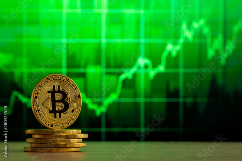 physical bitcoin standing at a wood table in front of a Green graph. Bitcoin Bull Market concept. photo