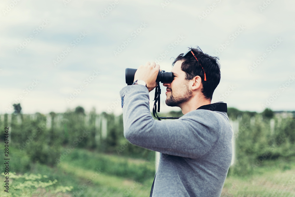 Portrait of young adventure man travelling with binoculars, watching landscape view outdoors. Young brunette man discover nature scenes. Travelling, discovering, vacation concept