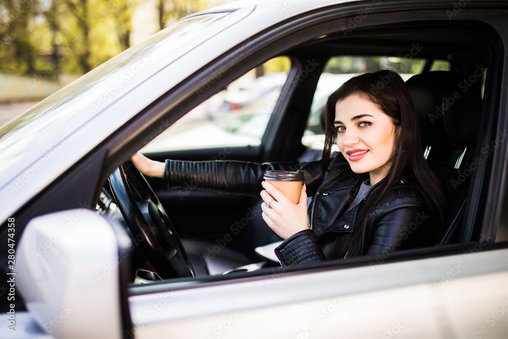 Young beauty woman in formal wear driving a car and holding a cup of coffee