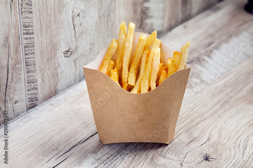 Close up view on Potatoes French Fries in Carton Package Box Isolated on wooden background. Fast food concept mock up. Blank kraft or craft paper cardboard with french fries fry