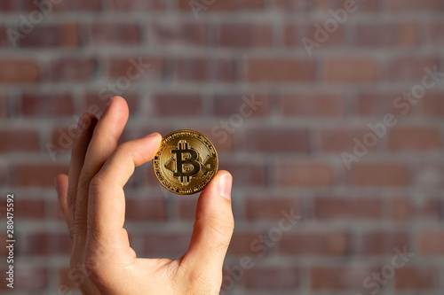 man hand holding a physical bitcoin in front of a brick wall photo