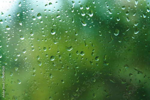 Beautiful view from window at dim outlines nature backdrop. Water drops on glass with blurred edges. View from window on rainy day. Rain drop on windowpane with blur tree background.