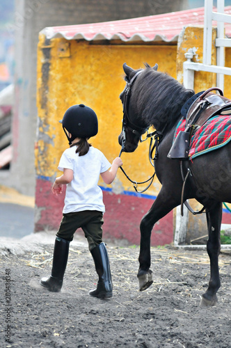 Small jockey girl takes horse to stable after riding session