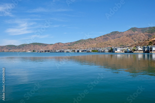 mountains and inn houses along the blue Erhai lake in Shuanglang Yunnan China. Symmetrical reflection in peaceful water. Sunny blue sky white clouds. Famous tourist attraction photo