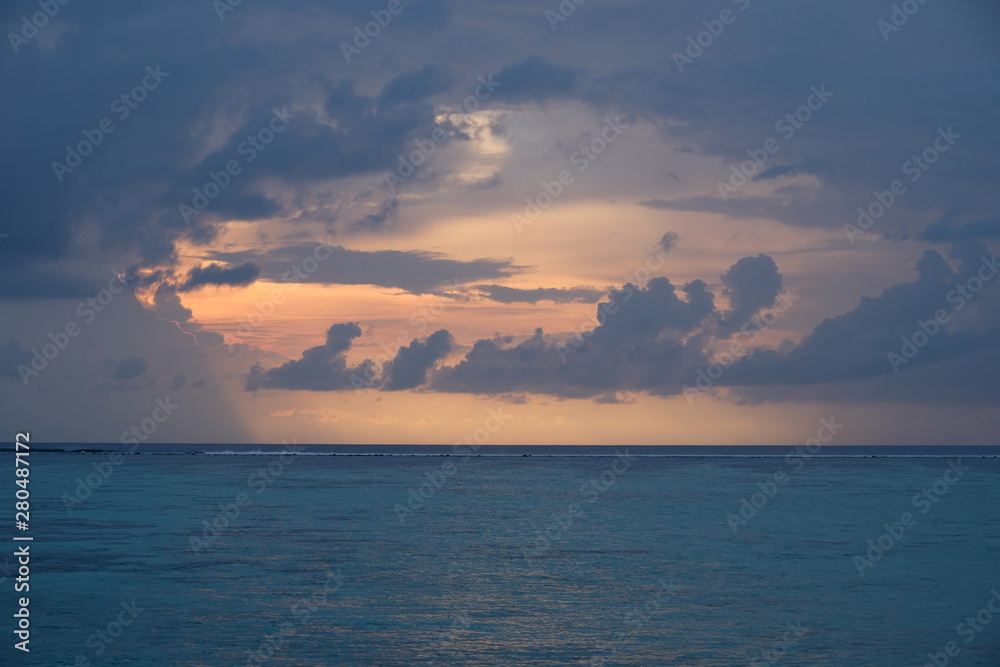 orange sunrise in cloudy blue sky of maldives. Blue peaceful sea ocean waves on horizon