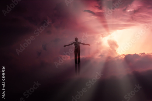 Silhouette of a man flying up in the sky in the bright rays of the sun with arms spread apart.