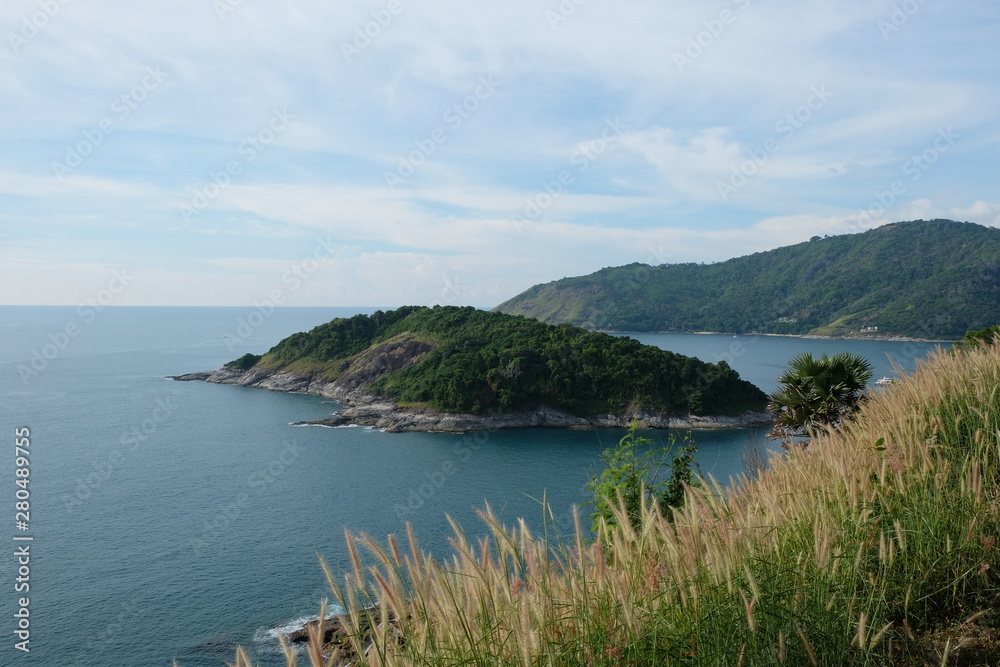 Prom thep cape island in sea south of Phuket Island Thailand. Blue sunny cloudy sky and wide ocean water. brown reeds as foreground