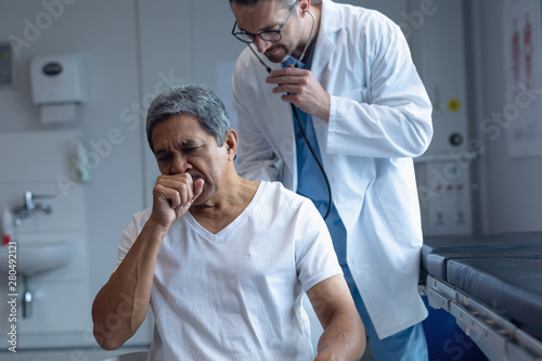 Male doctor examining patient with stethoscope in hospital