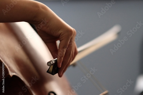 Close up one musician's hand taking a bow, playing brown cello. Daylight reflection on wood. Blurred background