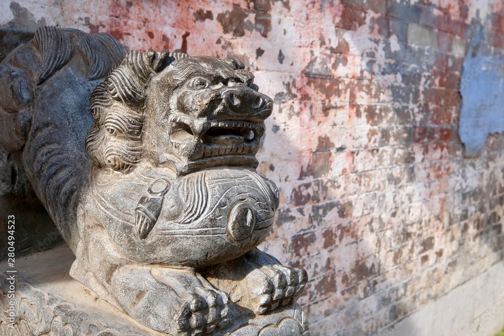 close up one grey traditional Chinese stone lion in front of blurred mottled wall under sunshine close up one grey traditional Chinese stone lion in front of blurred mottled wall under sunshine