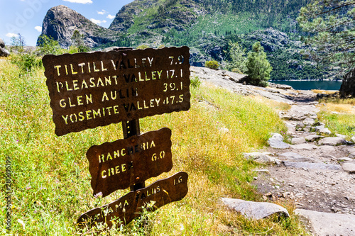 Hiking trail sign posted on the Wapama Falls trail, on the shoreline of Hetch Hetchy reservoir, showing points of interest and distances; Yosemite National Park, Sierra Nevada mountains, California photo