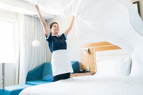 Happy Housekeeping Maid Making Bed In Hotel