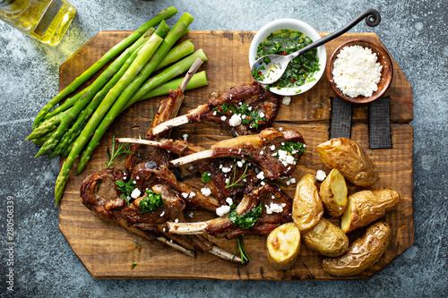 Grilled lamb chops with green herb sauce, feta, asparagus and potatoes served on a wooden board