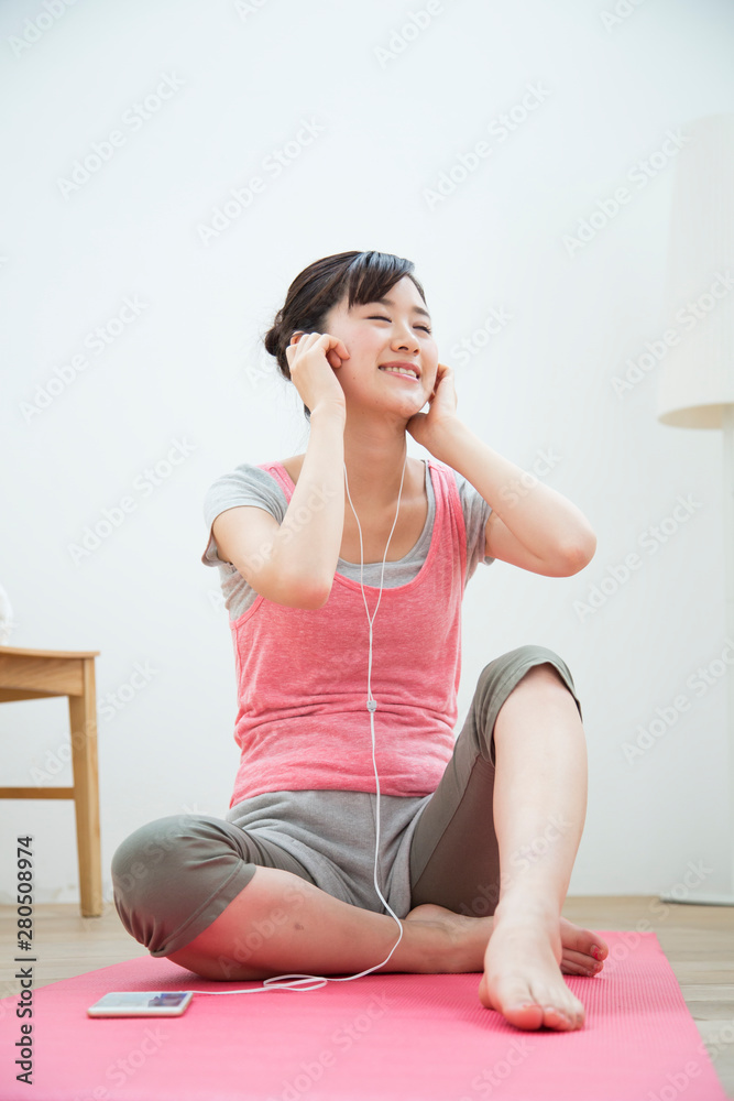 ヨガマットに座って音楽を聴く女性 ヨガマットに座って音楽を聴く女性